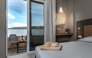 Habitación de hotel con cama, una silla, una mesa con una botella y vasos, un espejo y vistas al exterior.