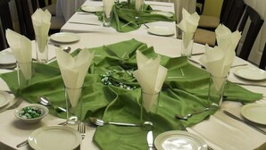 Un comedor con mesas redondas dispuestas para una comida, con manteles verdes, servilletas blancas y centros de mesa florales.