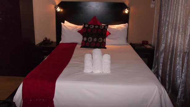 Una cama bien hecha con sábanas blancas, un plaid rojo y una almohada decorativa con estampado de lunares.