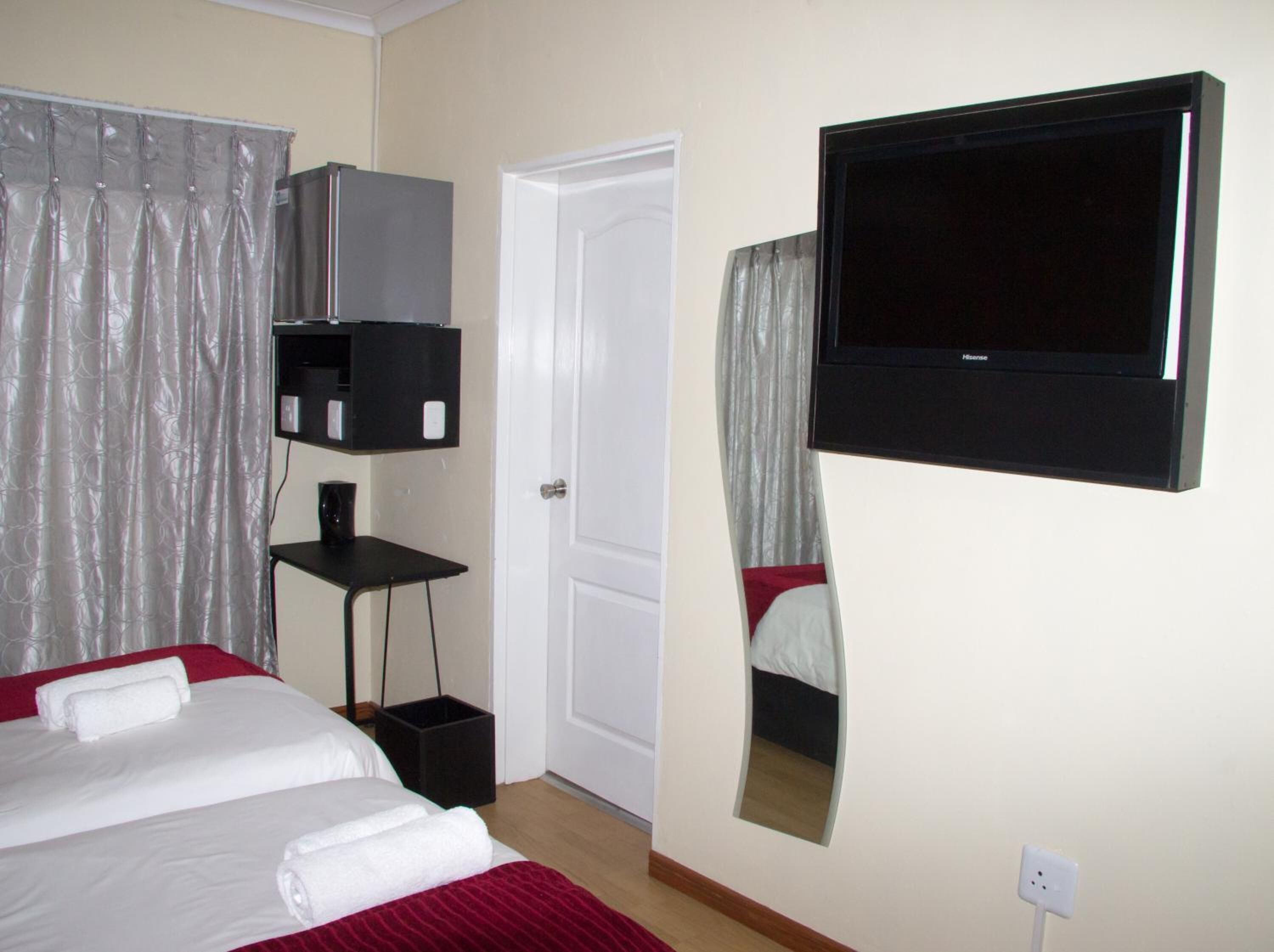 A hotel room with a bed, a TV mounted on the wall, a door, and a small table with a speaker.