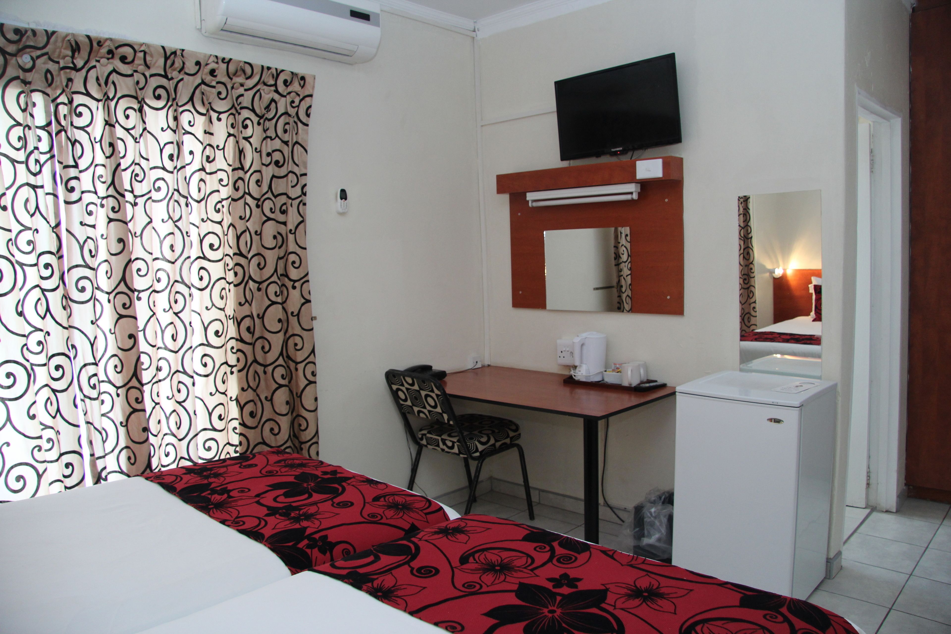 Una habitación de hotel con cama, escritorio, silla, televisor, espejo y refrigerador.
