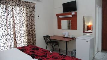 Una habitación de hotel con cama, escritorio, silla, televisor, espejo y refrigerador.