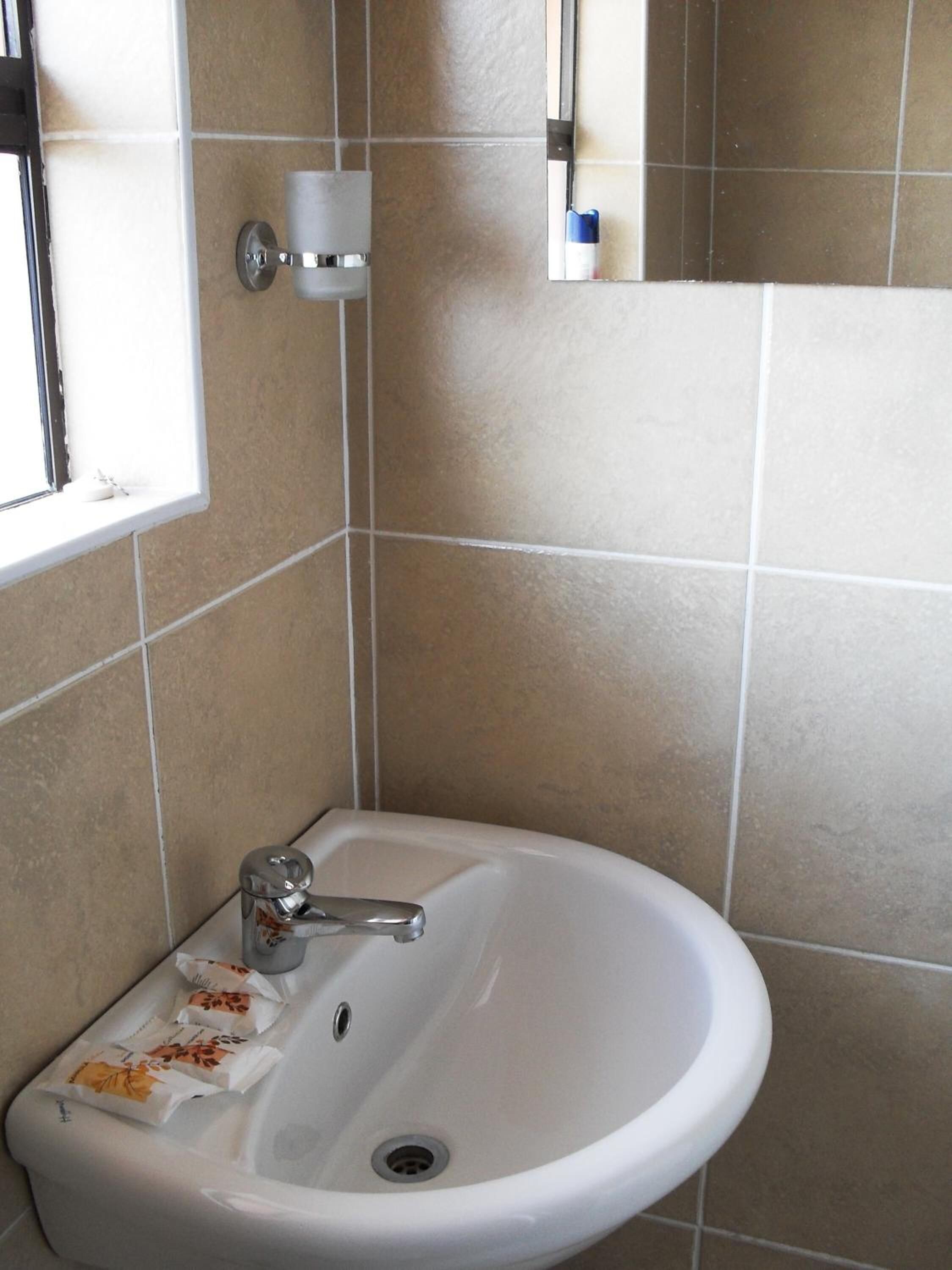 Une salle de bain avec un lavabo blanc, une fenêtre et un miroir au mur.