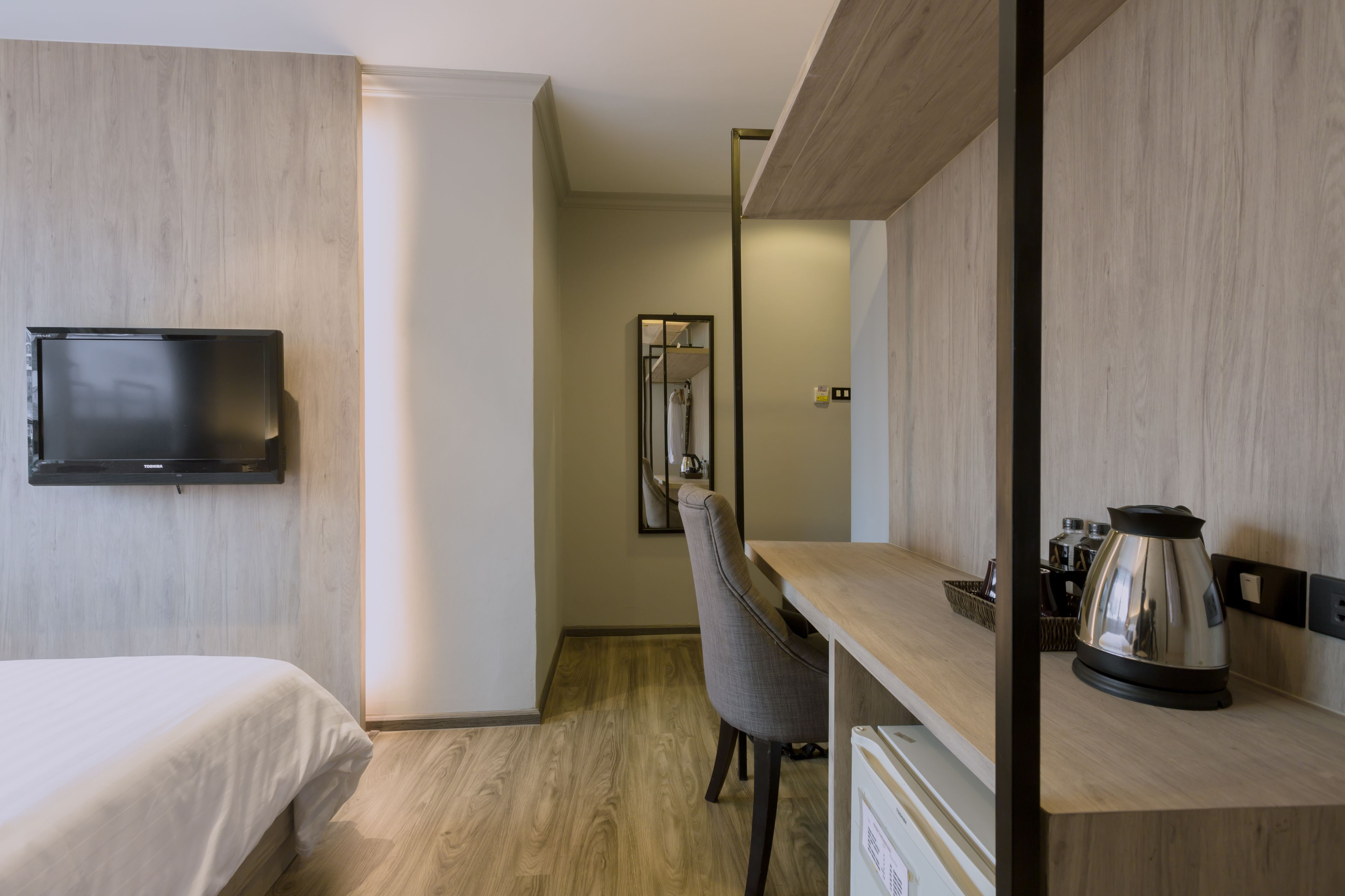 A hotel room with a bed, a desk with a chair, a kettle, and a television mounted on the wall.
