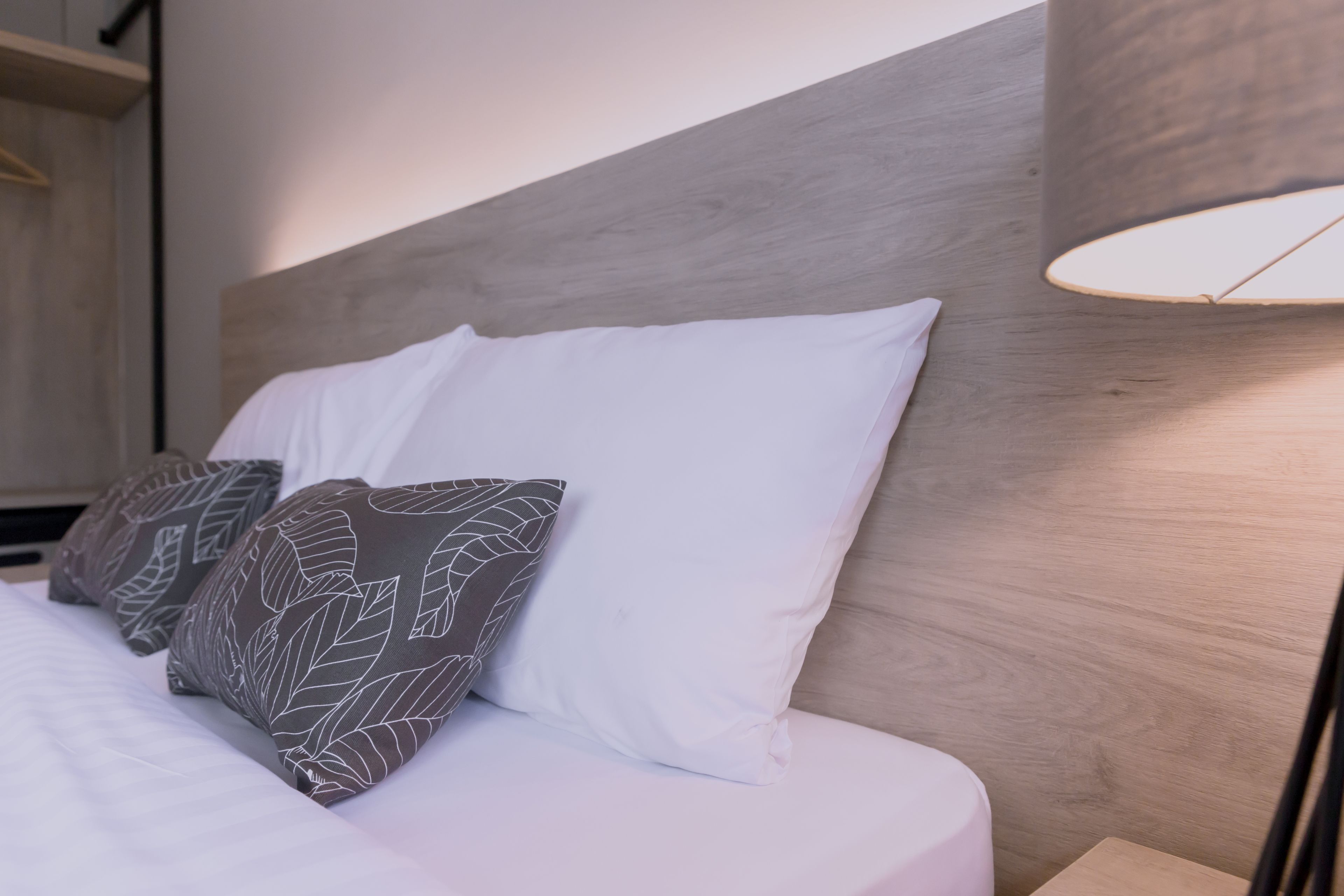 Un lit bien fait, avec des oreillers blancs et à motifs, une tête de lit en bois et une lampe de chevet.