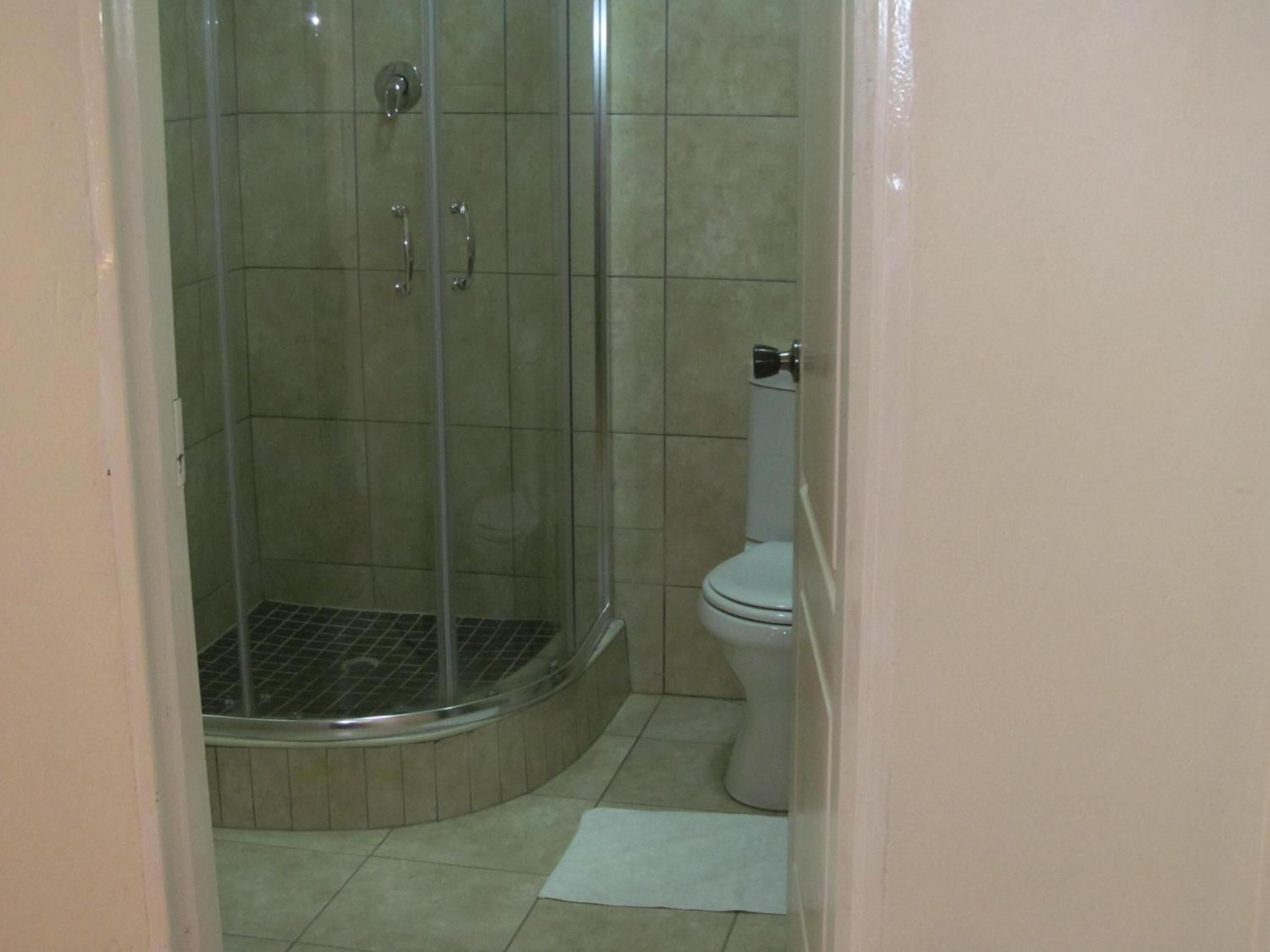 Un baño con ducha de vidrio, inodoro y una pequeña alfombra en el suelo.