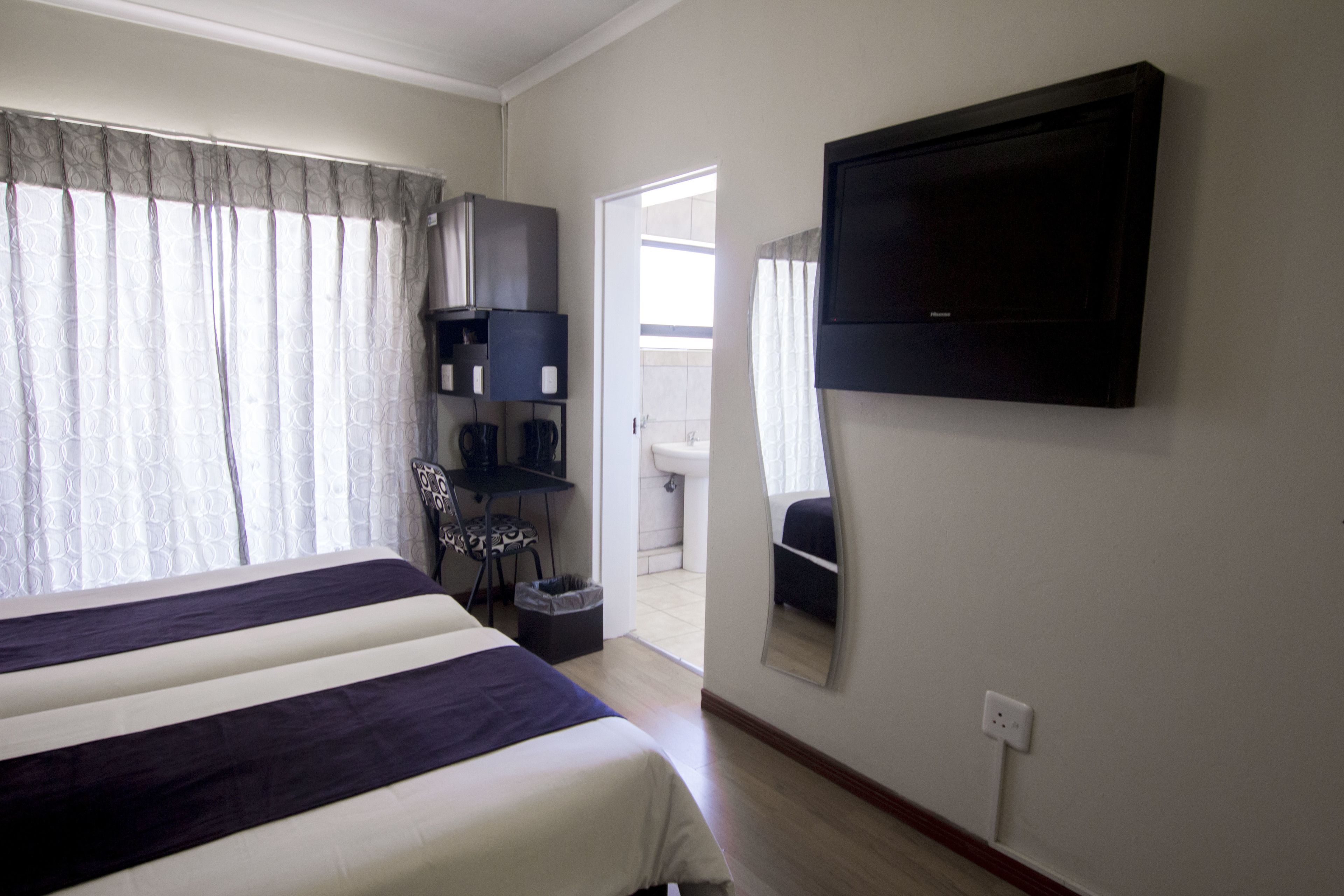 Ein Hotelzimmer mit Bett, einem an der Wand befestigten Fernseher, einem Schreibtisch mit Stuhl und Blick ins Badezimmer.