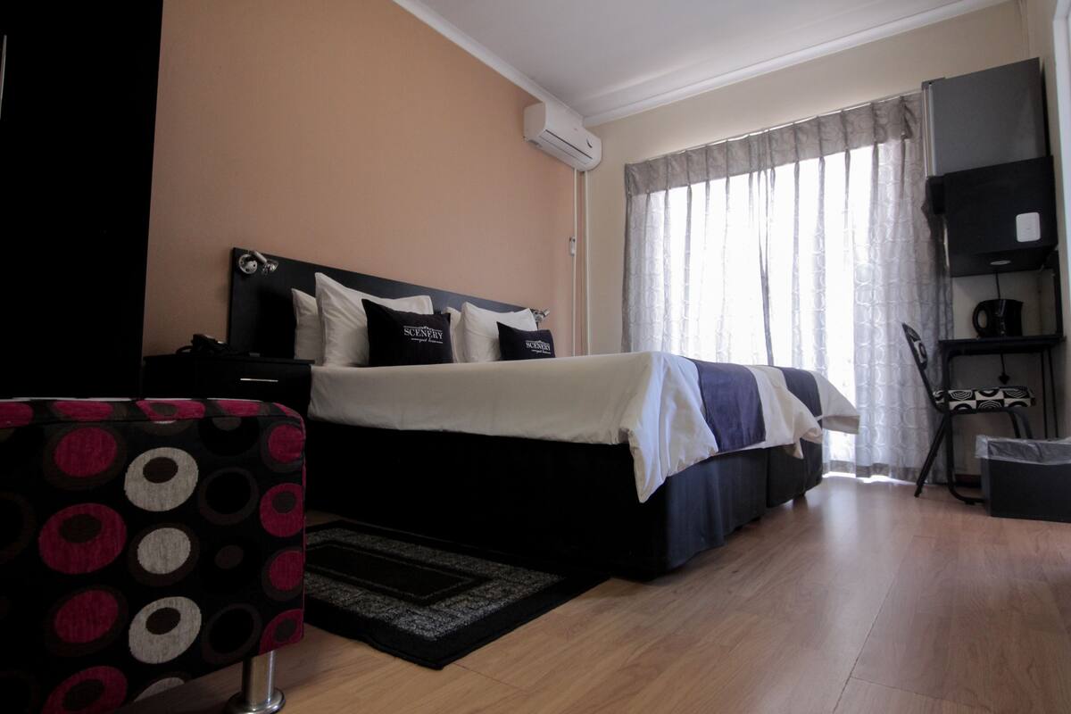A hotel room with a bed, a chair, a desk, and a window with curtains.
