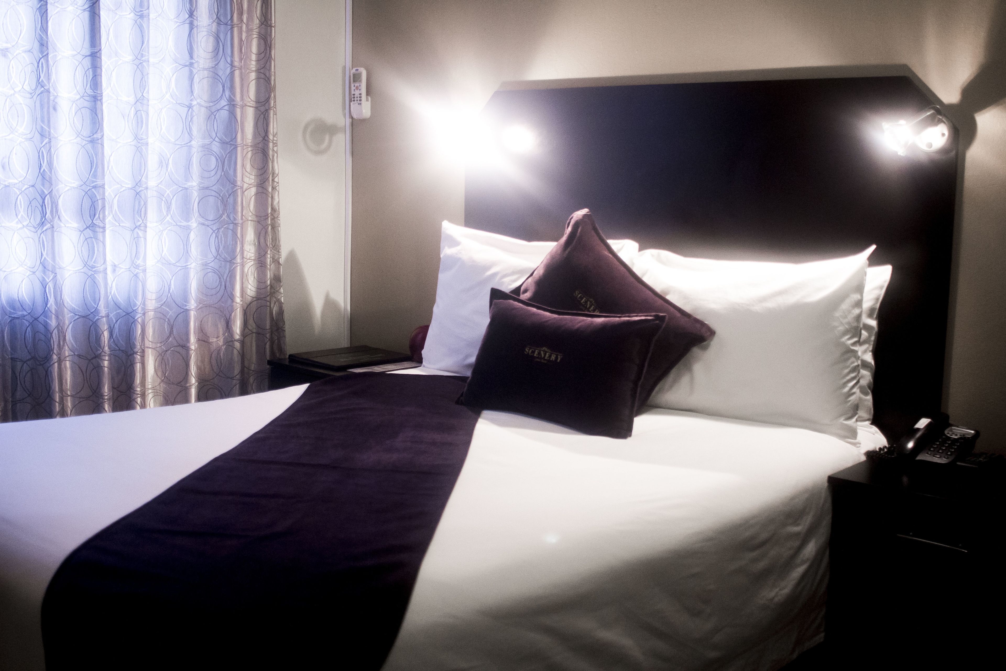 A hotel room with a bed, a nightstand, a telephone, and a curtain.