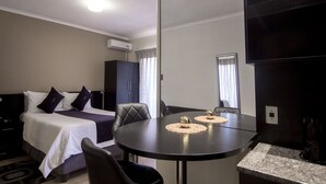 A hotel room with a bed, a dining table with placemats, a coffee maker, and a wardrobe.