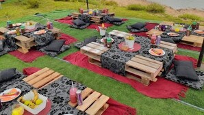 An outdoor dining area with tables set up on artificial grass, surrounded by a tent structure.