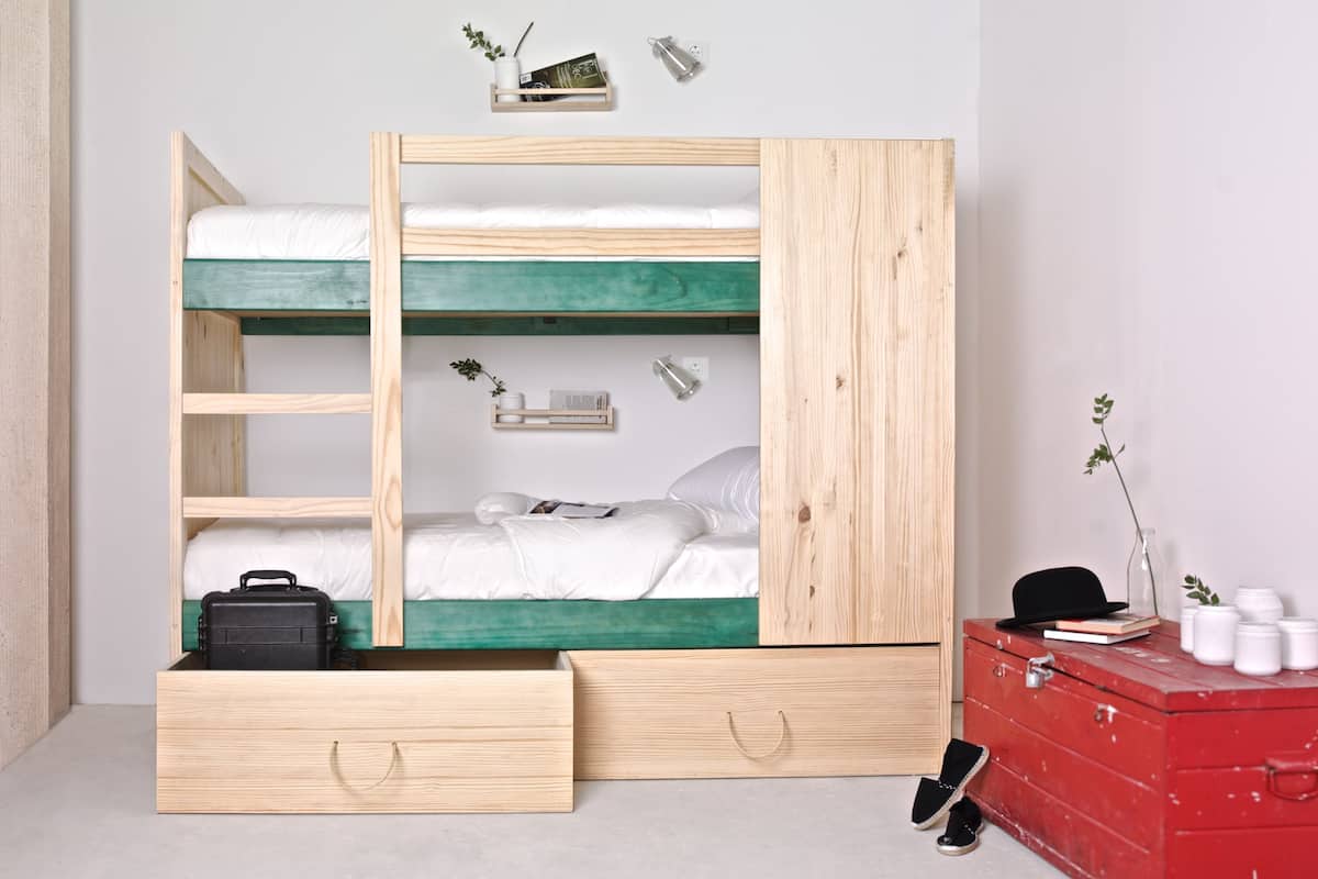 Una litera con cajones para guardar objetos, un pequeño estante con libros y una planta, y un aparador rojo con frascos.