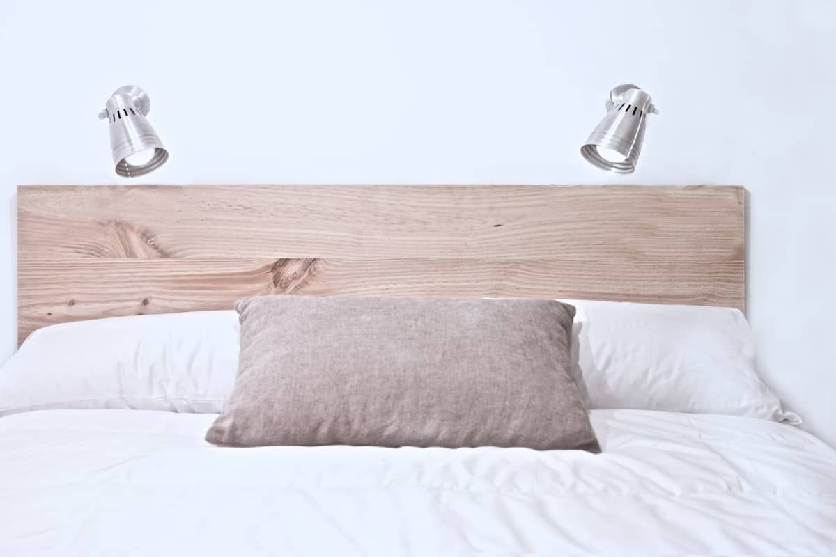 Una cama con ropa de cama blanca, un cabecero de madera y dos lámparas de noche.