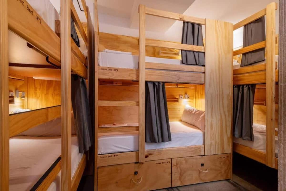Habitación con literas de madera, un escritorio pequeño y una ventana con cortinas.