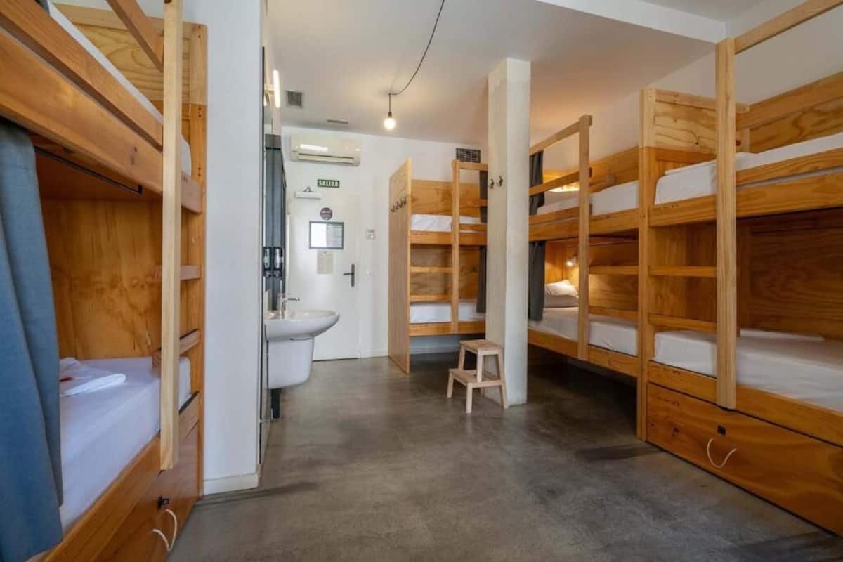 Habitación pequeña con literas, lavamanos y un taburete.