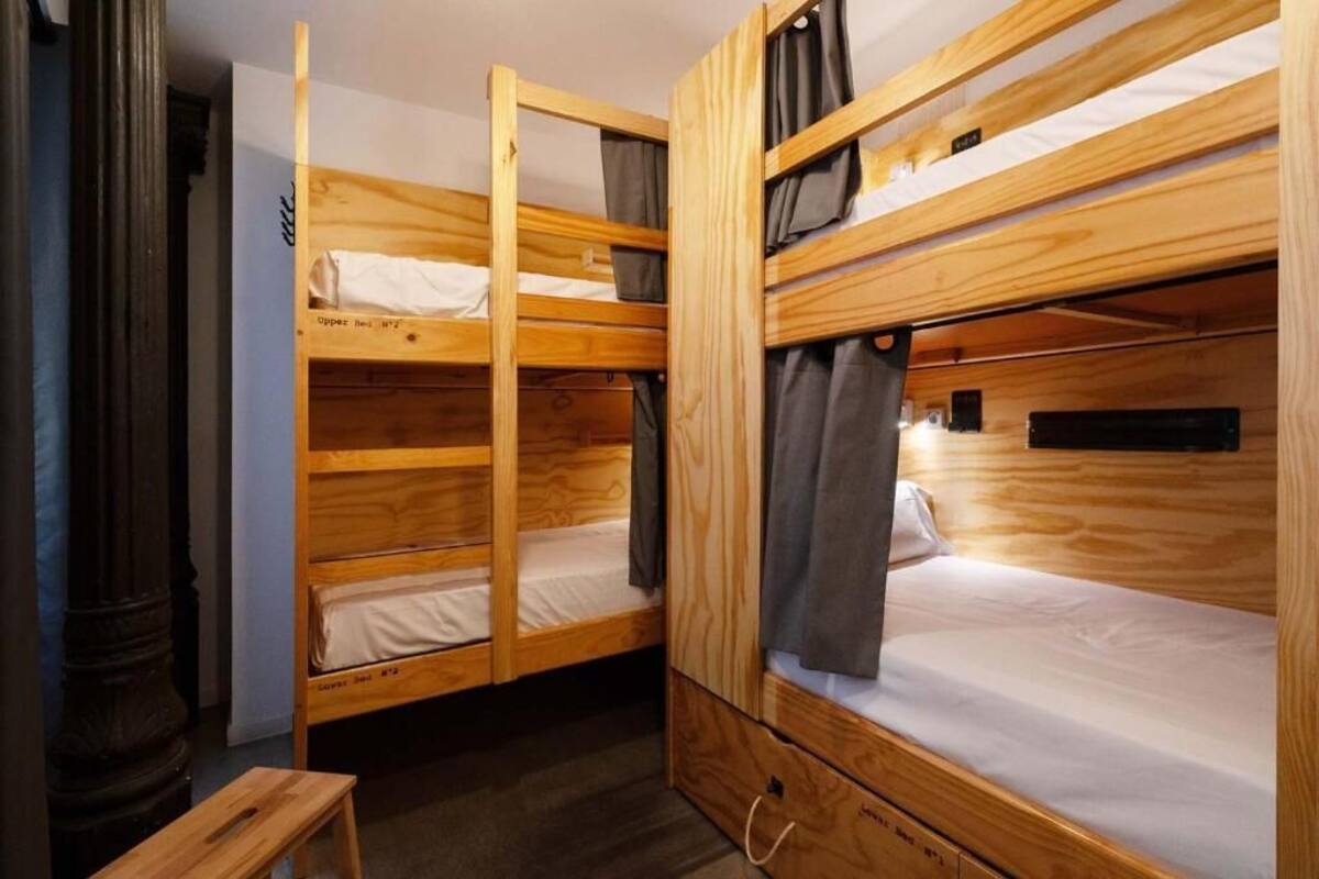 Habitación con literas de madera, una mesita pequeña y un armario.