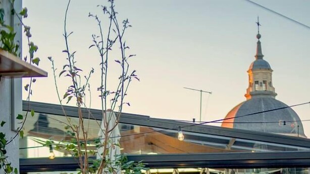 An outdoor seating area with tables and chairs, a glass wall, and a view of a building with a dome. - The Hat Madrid (Madrid)