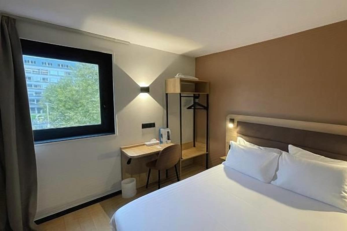 A hotel room with a bed, a desk, a chair, a wardrobe, and a window.
