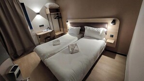Quarto de hotel com uma cama de casal, uma escrivaninha e uma cadeira.