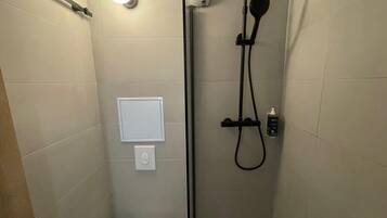 Un baño pequeño y moderno con inodoro, ducha y dispensador de jabón de pared.