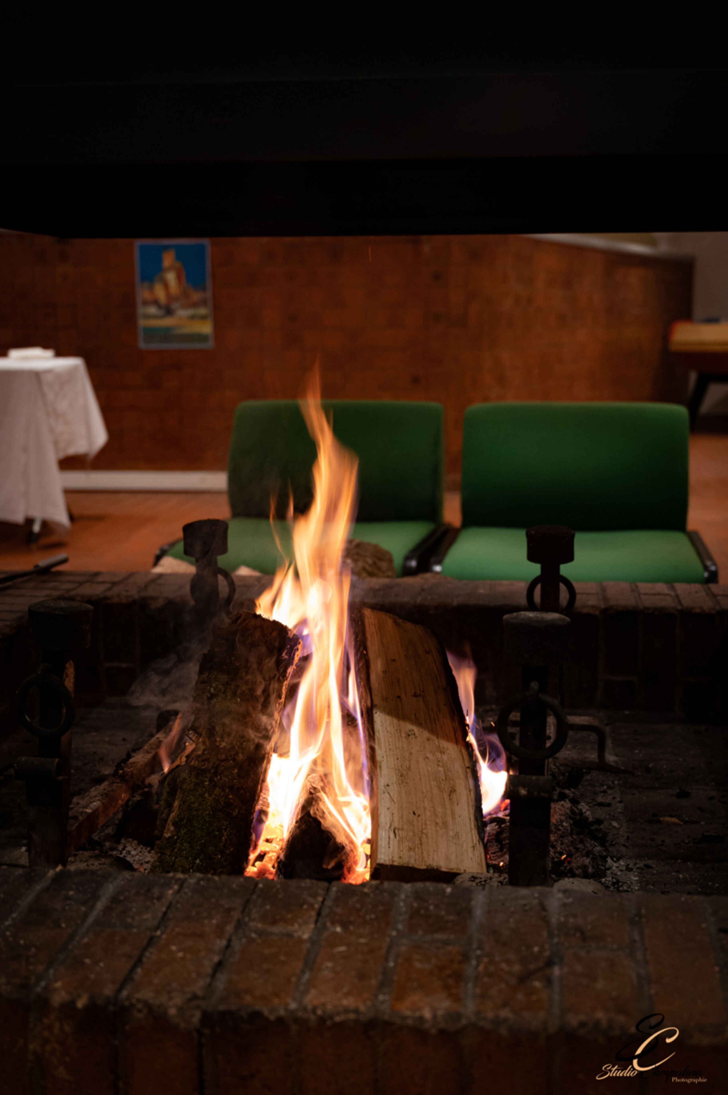 Una chimenea con leña ardiendo en una habitación con asientos tapizados en verde y una mesa con mantel blanco.