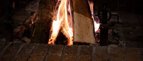 Una chimenea con leña ardiendo en una habitación con asientos tapizados en verde y una mesa con mantel blanco.