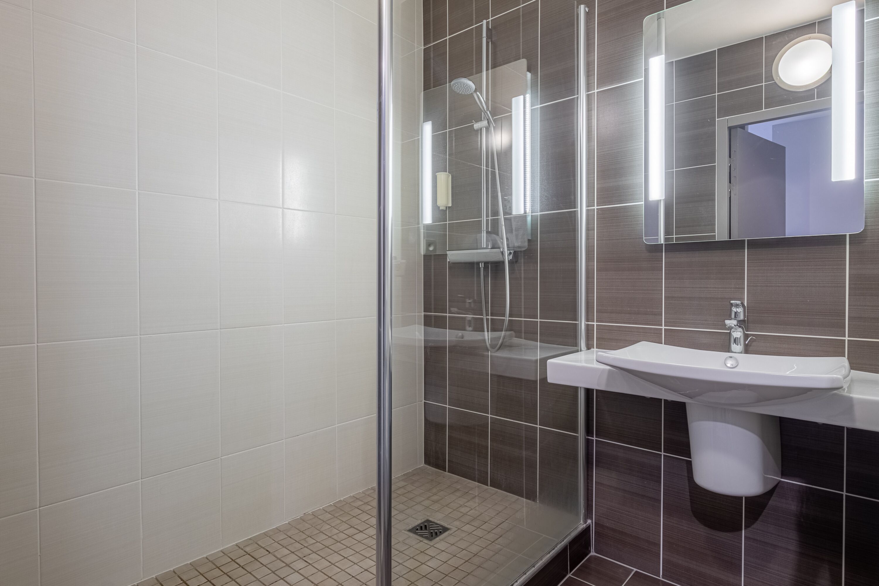A modern bathroom with a glass-enclosed shower, a white sink, and a mirror with integrated lighting.