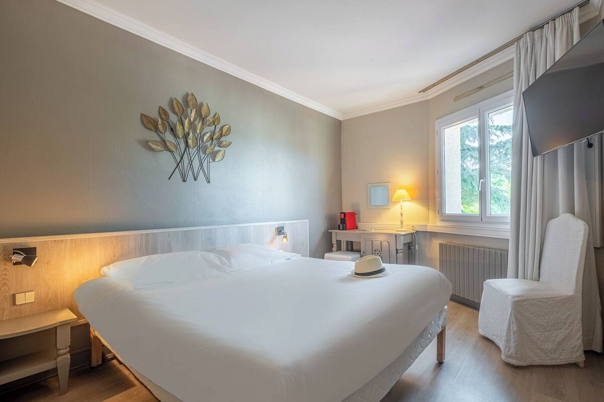 Une chambre d’hôtel avec un grand lit, une table de chevet, une lampe, une chaise et un élément décoratif mural.