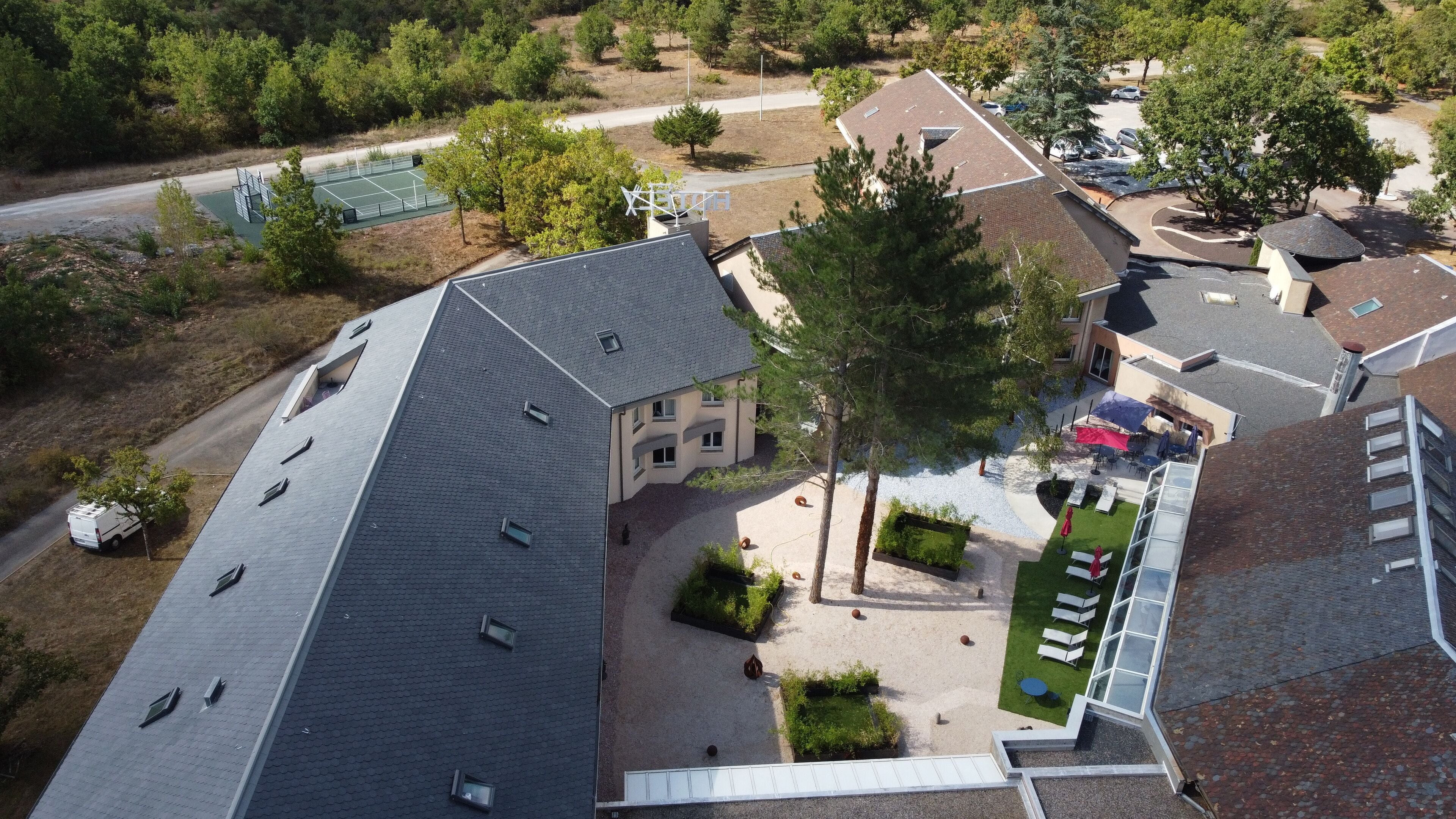 A residential area with a house featuring a sloped roof, a tennis court, and a parking area.