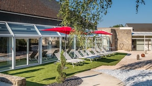 Een moderne buitenlounge met glazen wanden, rode parasols en ligbedden.