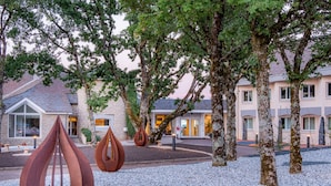 Een hotel binnenplaats met bomen, een grindpad en moderne metalen sculpturen.