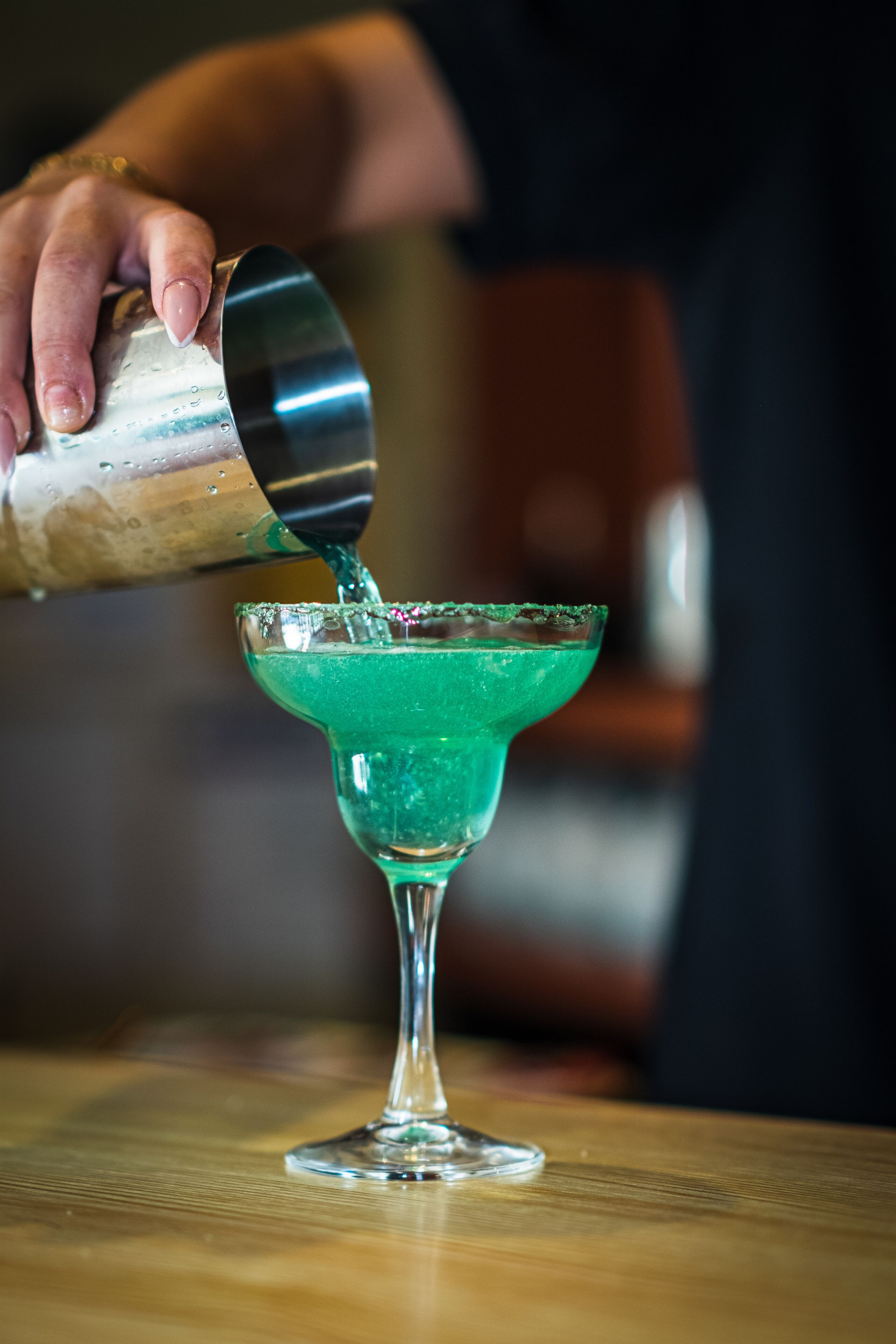 Una persona vertiendo un líquido verde en un vaso con borde metálico.