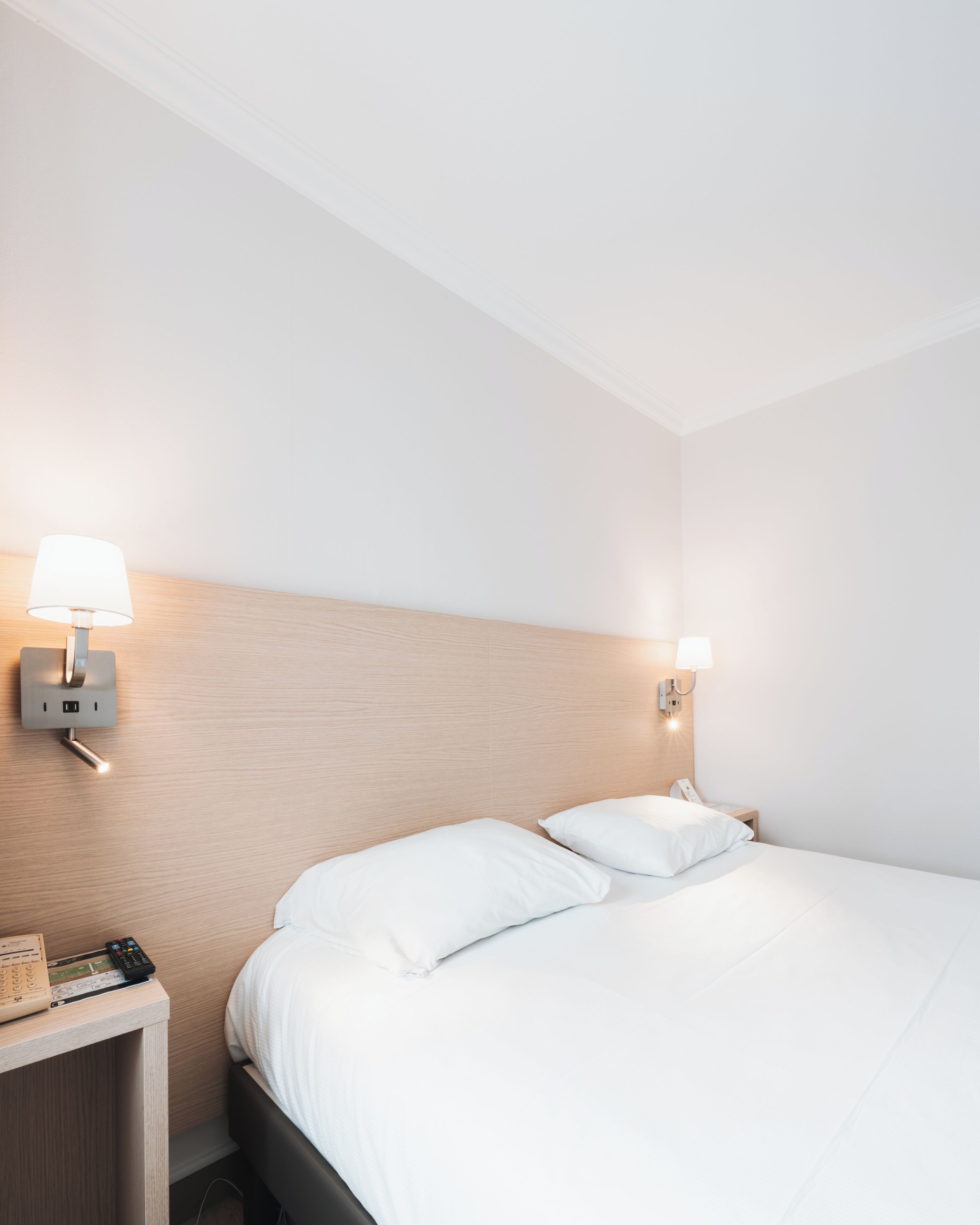 A hotel room with a bed, two bedside lamps, a nightstand, and a wall-mounted phone.