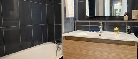 A modern bathroom with a white bathtub, a wooden vanity, a mirror, and a showerhead.