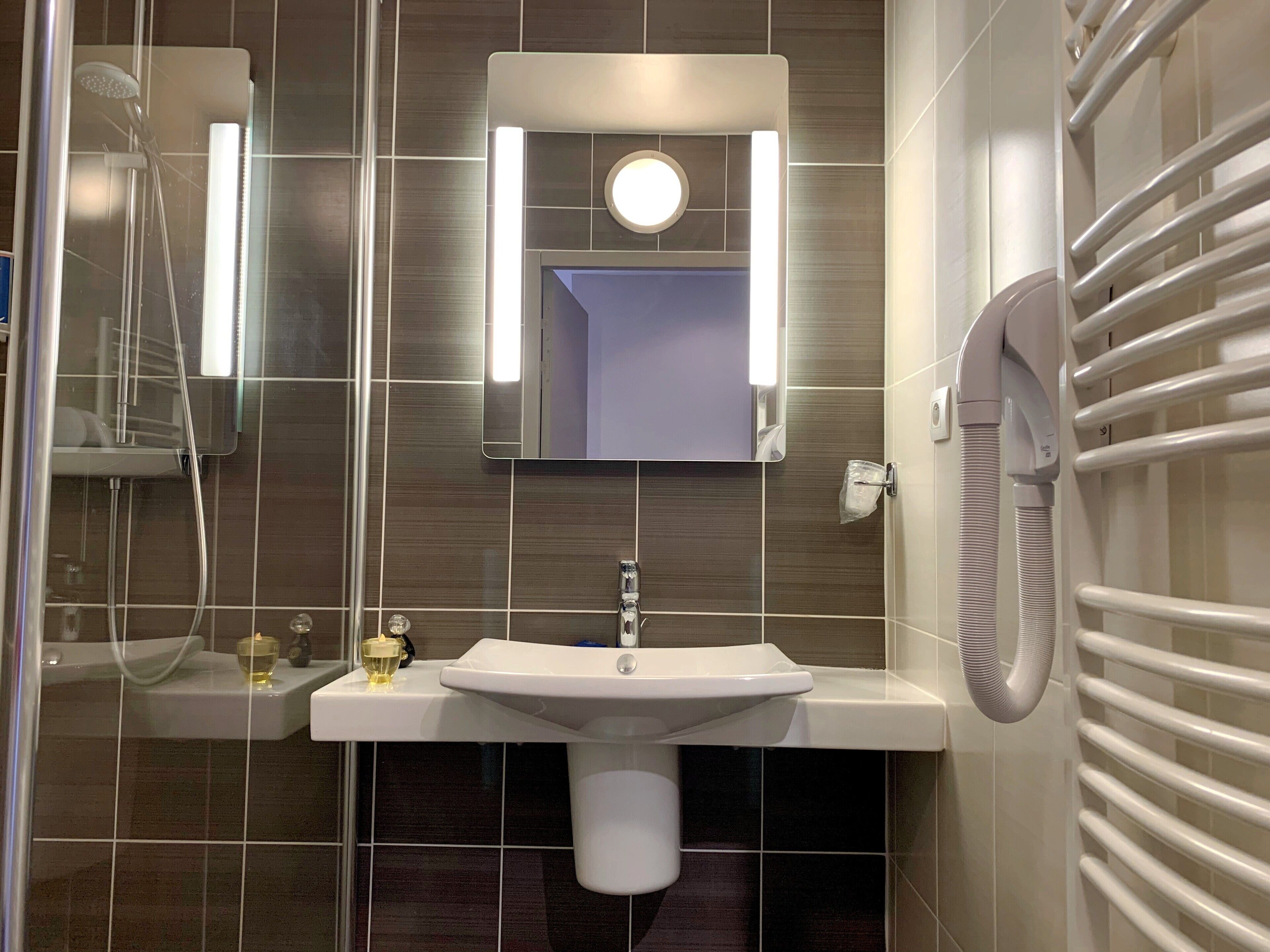 A modern bathroom with a white sink, a mirror, a handheld showerhead, and a towel rack.