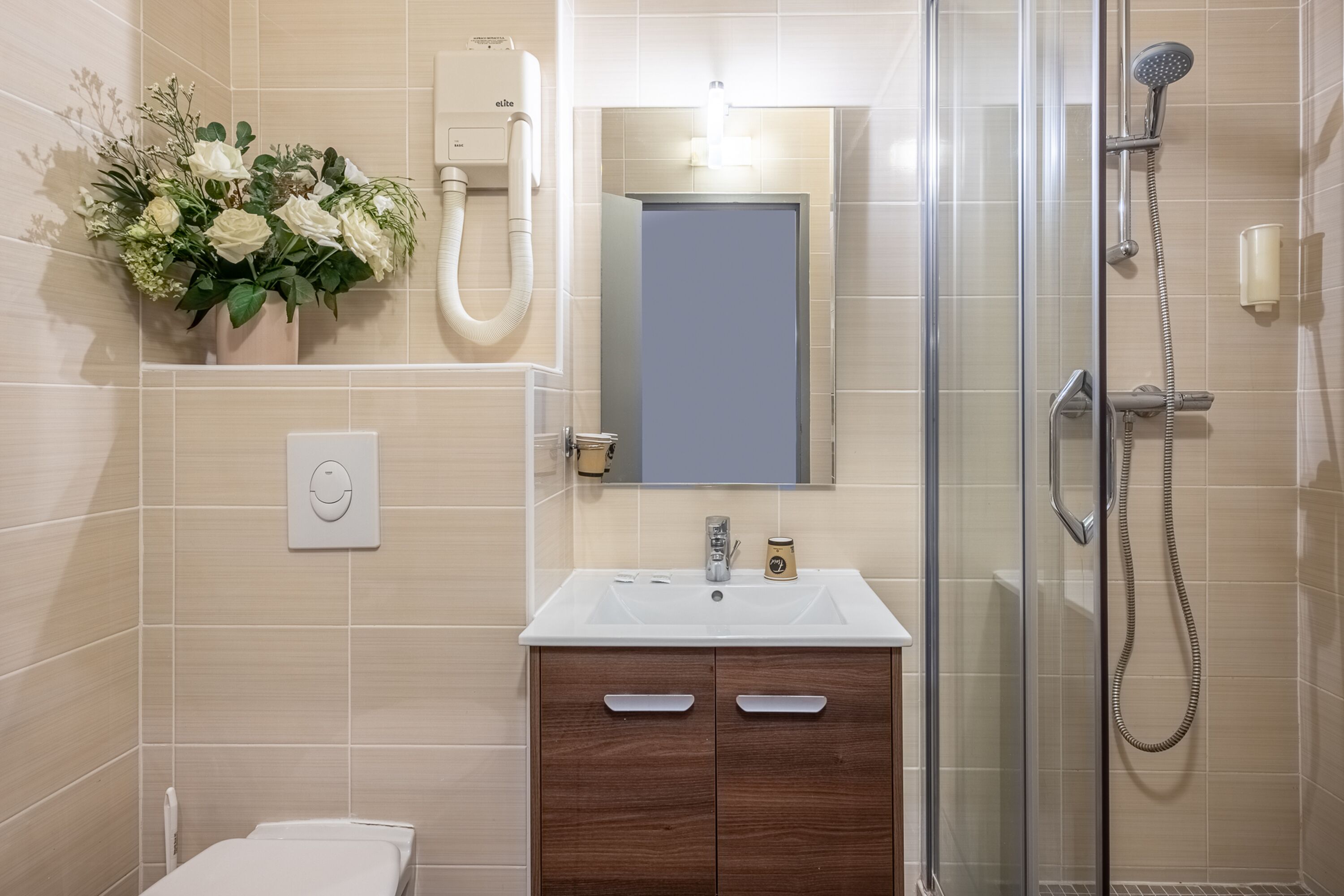 A bathroom with a glass shower enclosure, a white sink, a mirror, and a wooden cabinet.