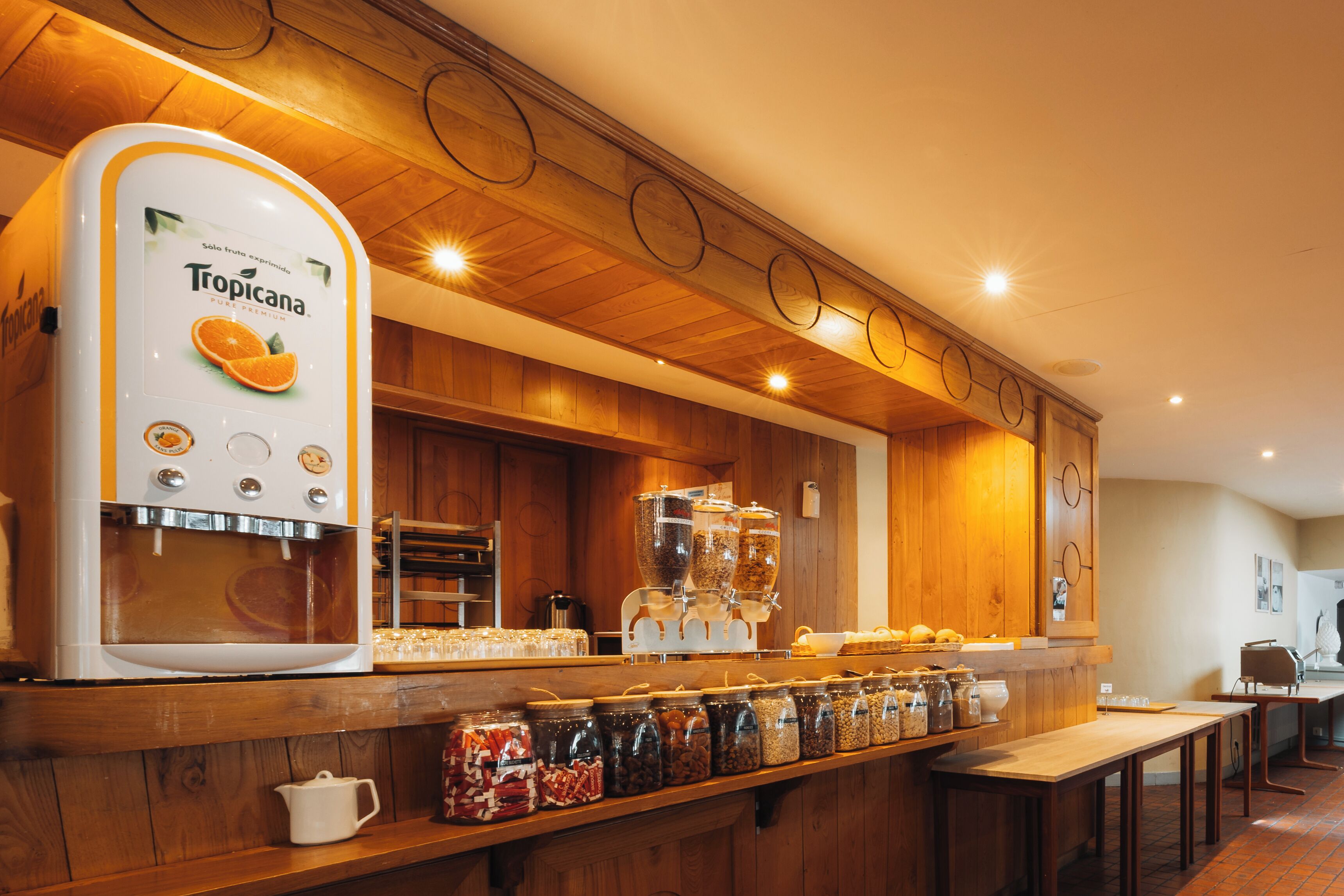 A coffee station with a Tropicana dispenser, various coffee machines, and a display of coffee beans.