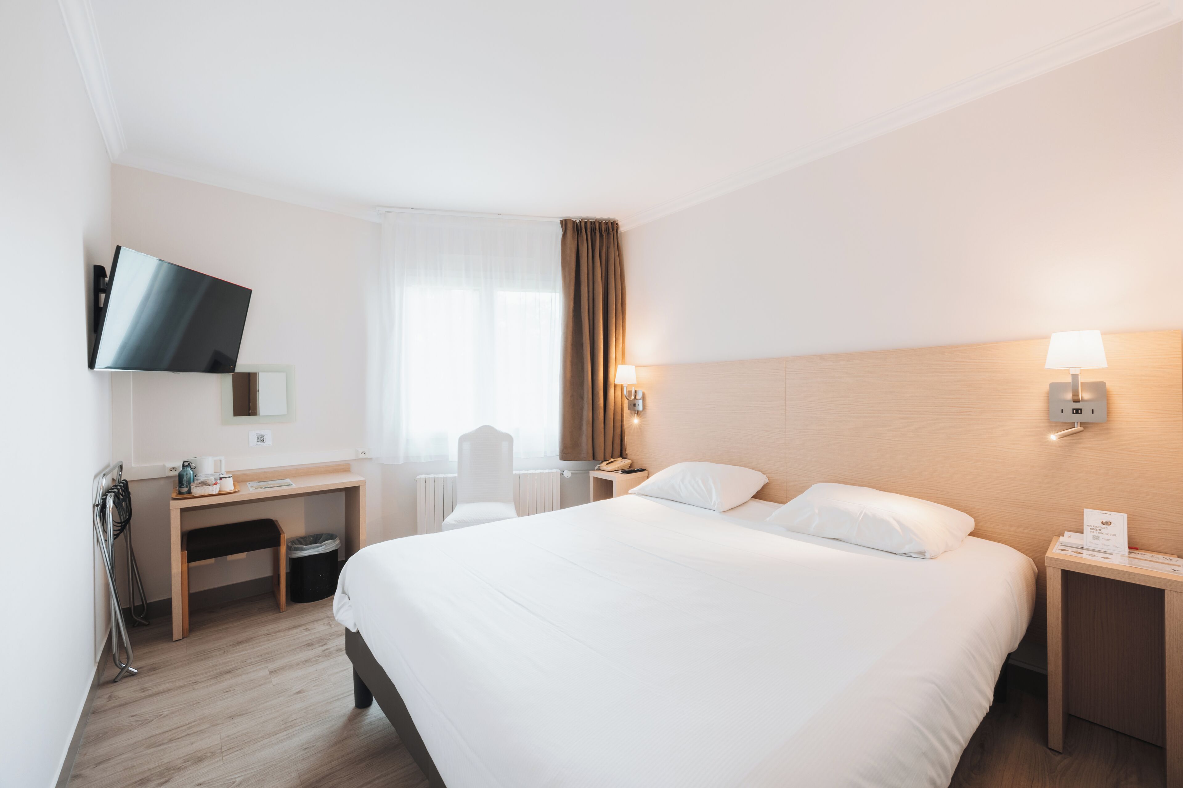 Une chambre d’hôtel avec un grand lit, un bureau, une chaise, un téléviseur fixé au mur et une table de chevet avec une lampe.
