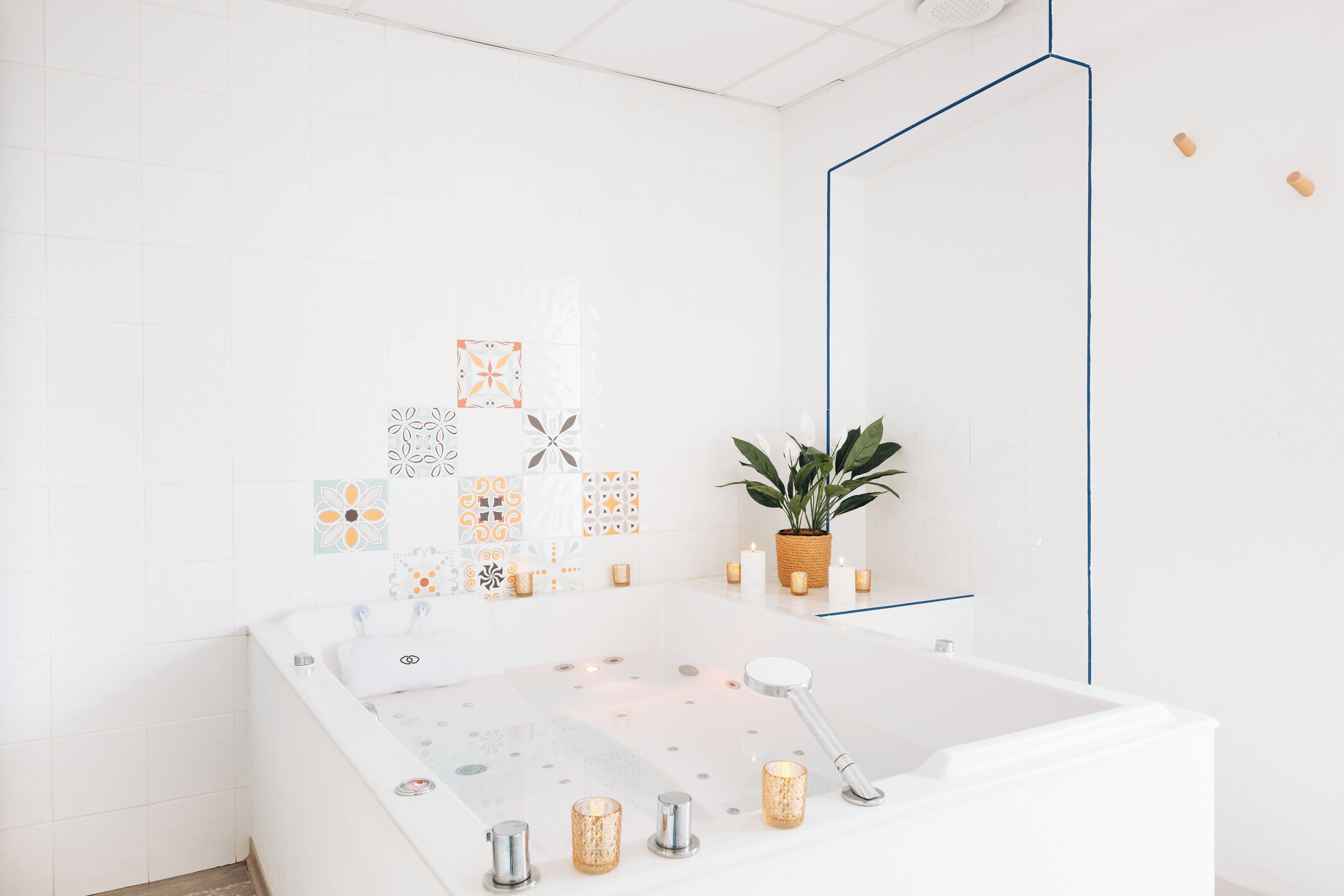A modern bathroom with a freestanding bathtub, decorative tiles, a potted plant, and candles.