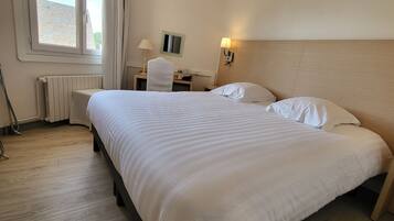 A hotel room with a large bed, a desk, a chair, a radiator, and a window with curtains.