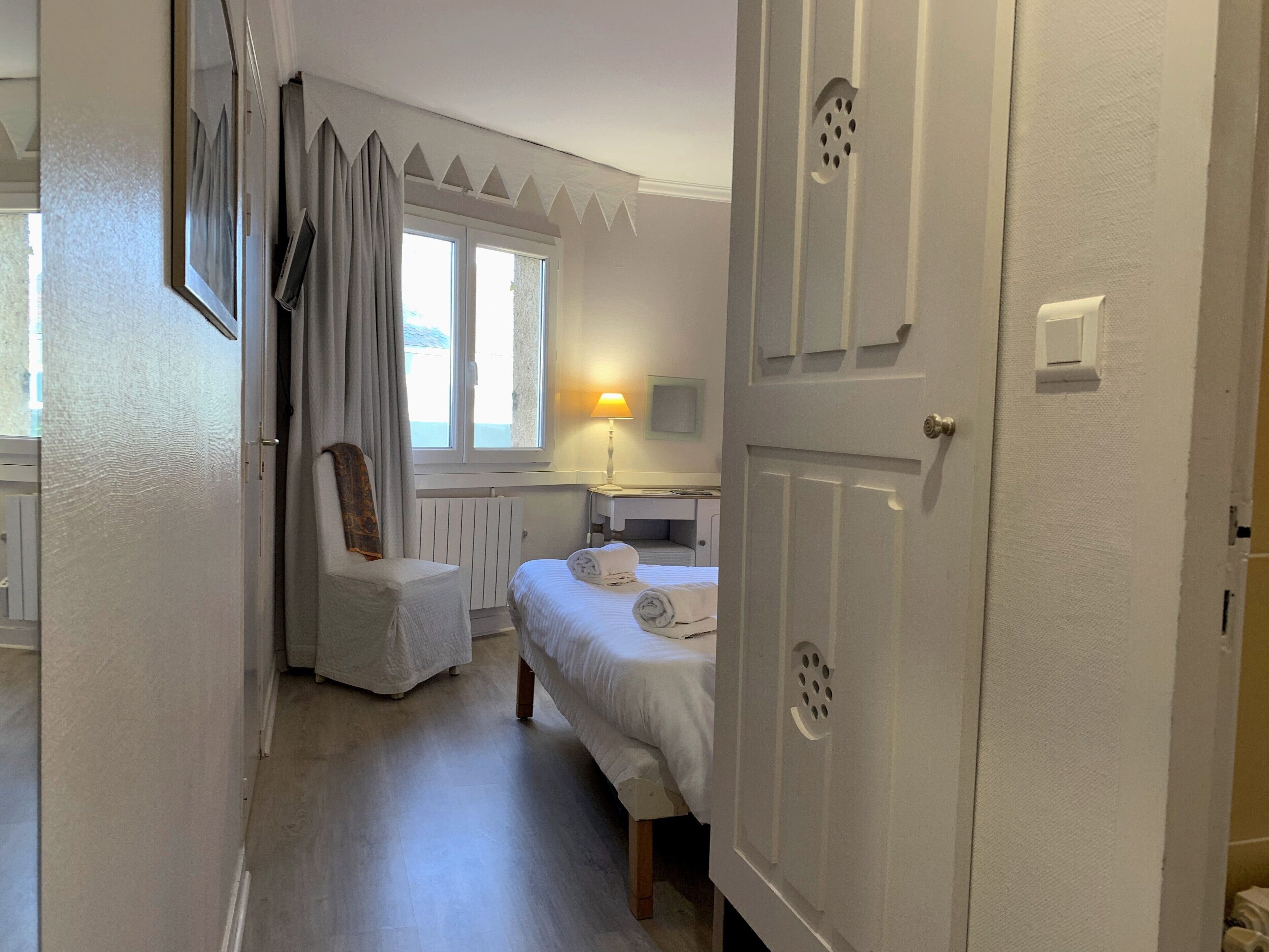 Et hotelværelse med seng, stol, skrivebord, lampe og vindue.