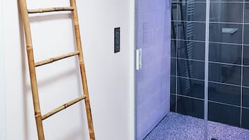 Een kamer met een houten ladder tegen een muur, een schuifdeur met een blauw betegelde binnenkant en een grijze vloer.