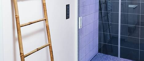 Una habitación con una escalera de madera apoyada en una pared, una puerta corredera con revestimiento de azulejos azules y un piso gris.