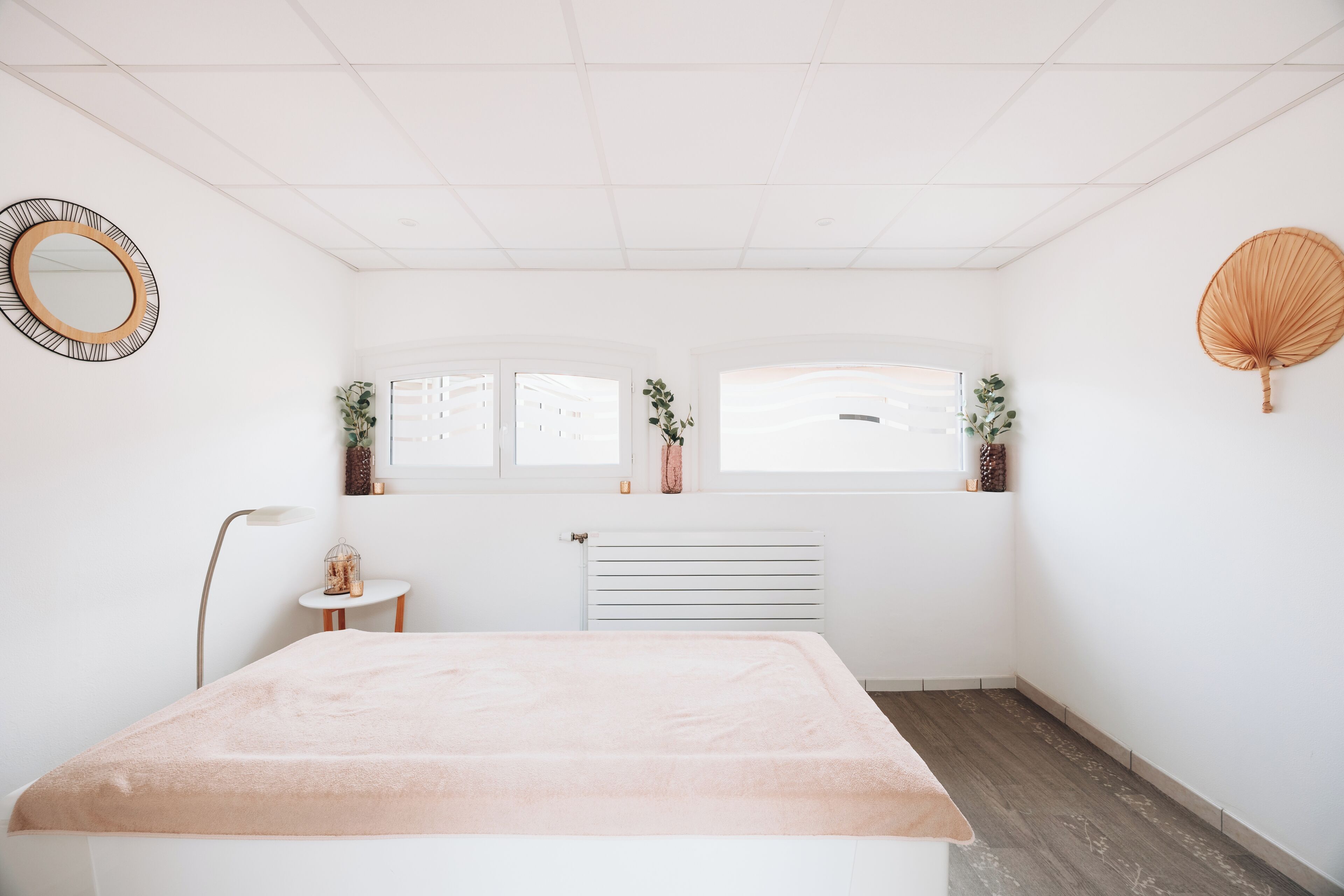 A minimalist bedroom with a bed, a radiator, a window with a view, a small table, and a floor lamp.