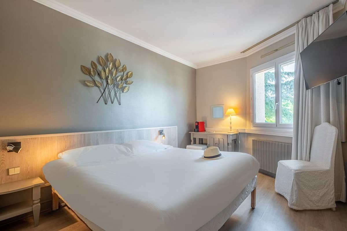 Une chambre d’hôtel avec un grand lit, des tables de chevet, un bureau, une chaise, une fenêtre avec des rideaux et un élément décoratif mural.