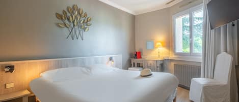 Habitación de hotel con una cama grande, una mesita de noche, una silla, una lámpara de pared, una ventana con cortinas y un adorno en la pared.