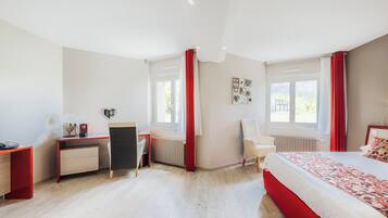 A modern bedroom with a bed, desk, chair, and large windows.