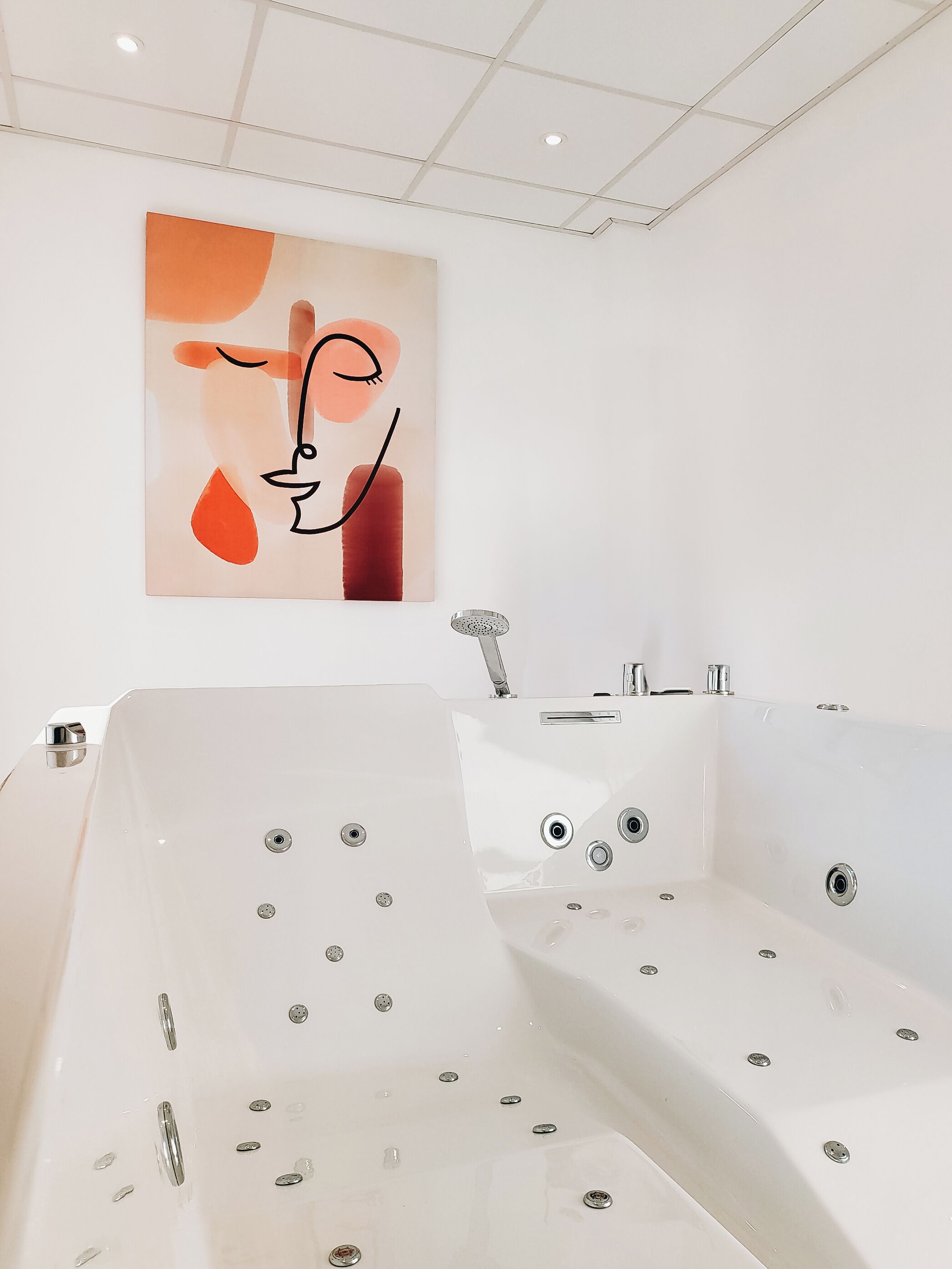 A modern bathroom with a large bathtub, a wall-mounted sink, and a ceiling light fixture.