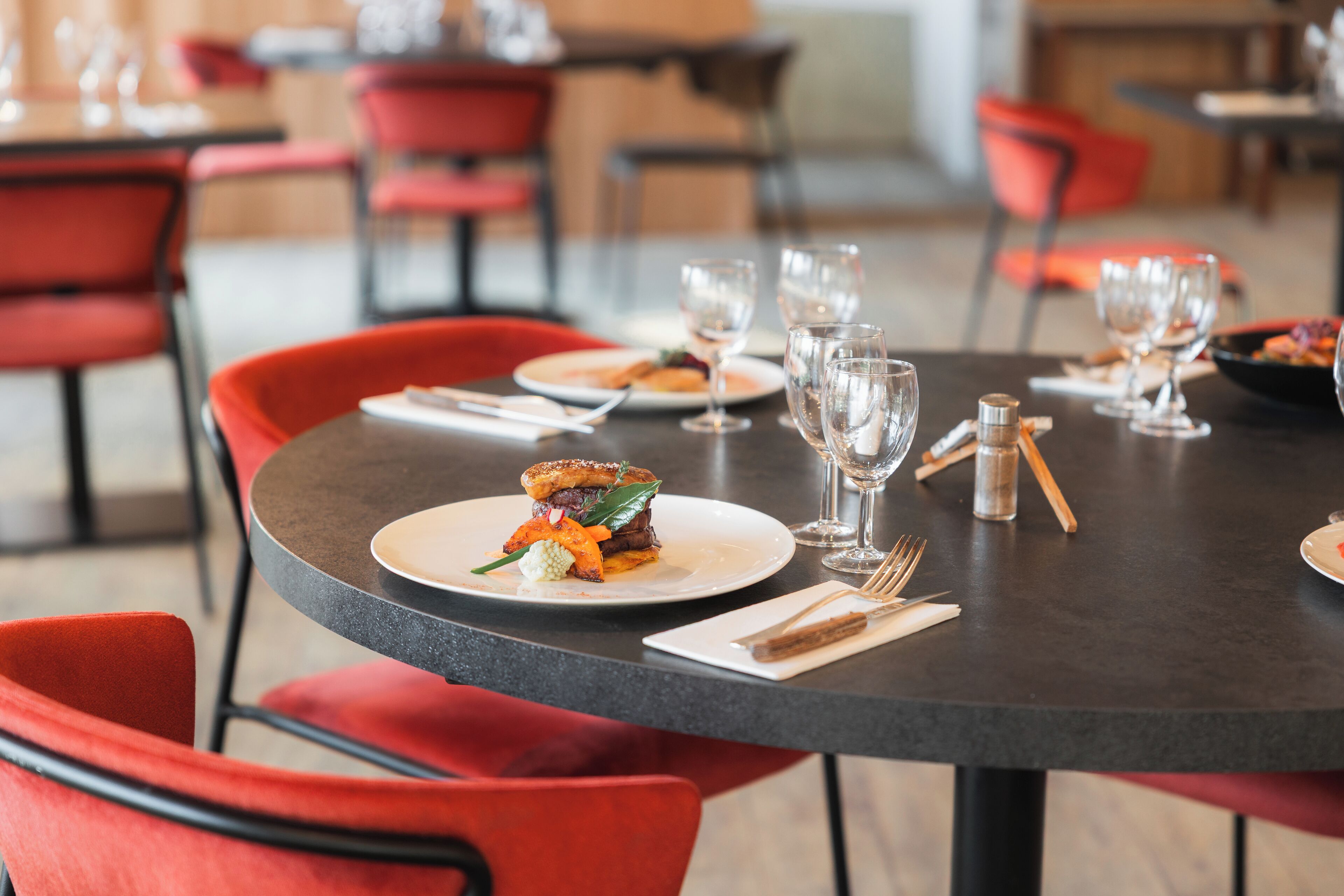 A dining table with plates of food, wine glasses, and cutlery.