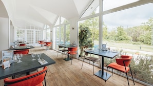 Een ruime eethoek met grote ramen, houten vloeren en rode stoelen.